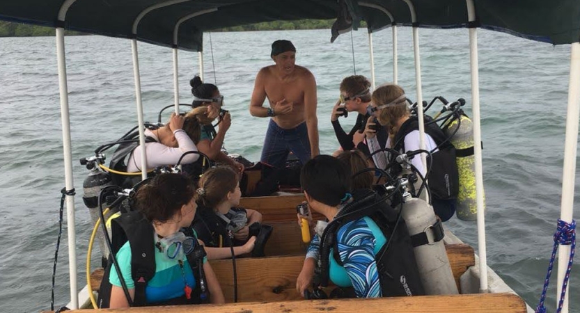 A group of people wearing scuba diving gear sit on a boat.